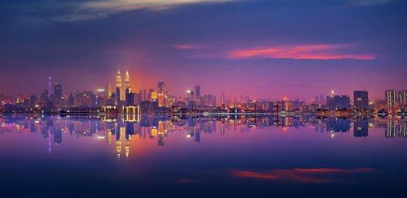 A panoramic shot of the city of Kuala Lumpur at night, seen from the water.